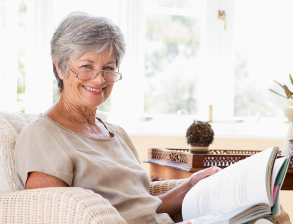 senior woman sitting in her living room on a sofa reading a book