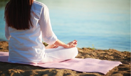 young woman sitting cross legged on the beach meditating