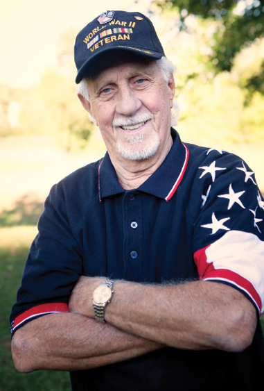 older adult man representing a Veteran standing with arms crossed smiling for photo